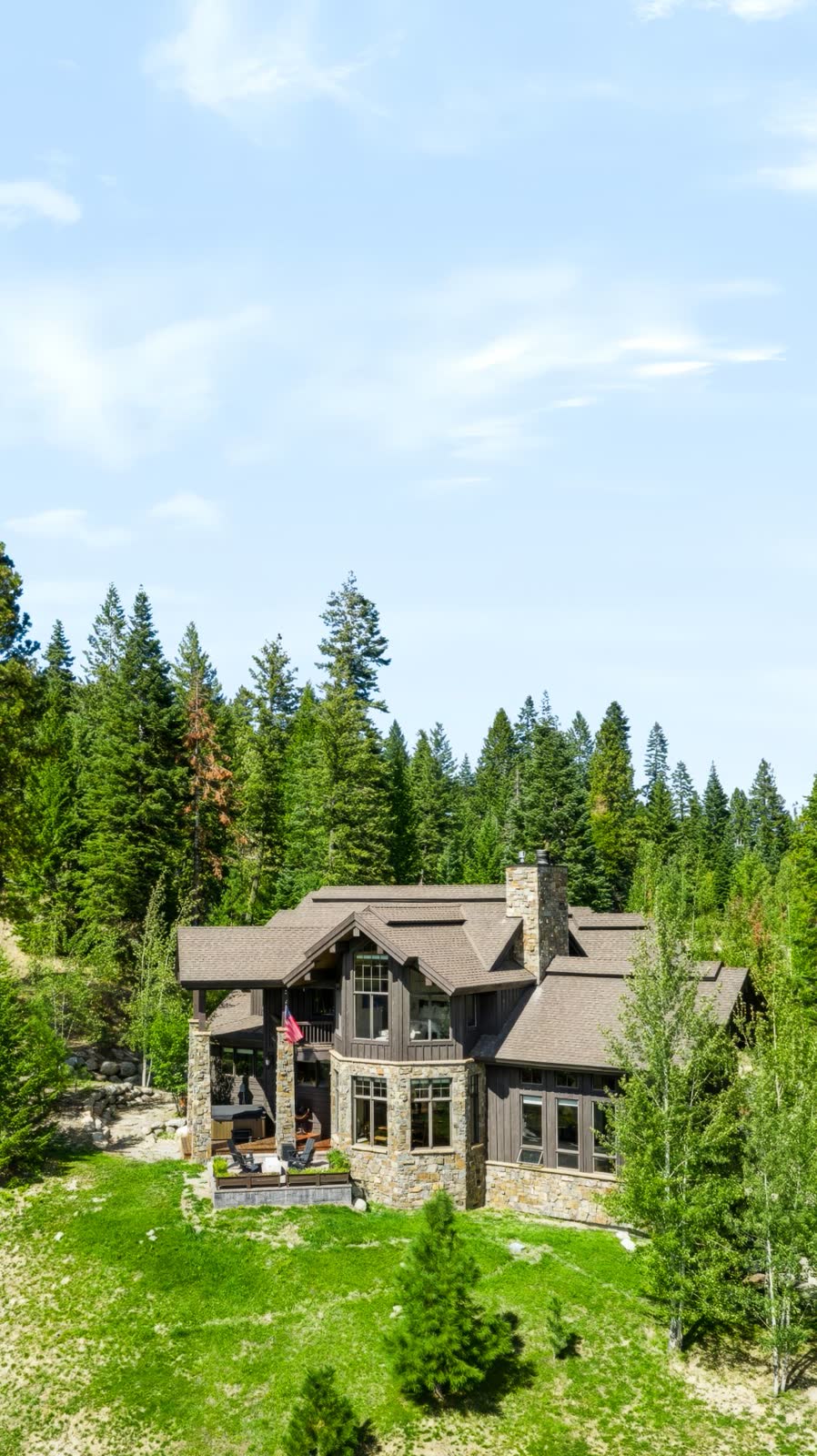 Vertical aerial view of a stone and timber cabin tucked into a pine forest